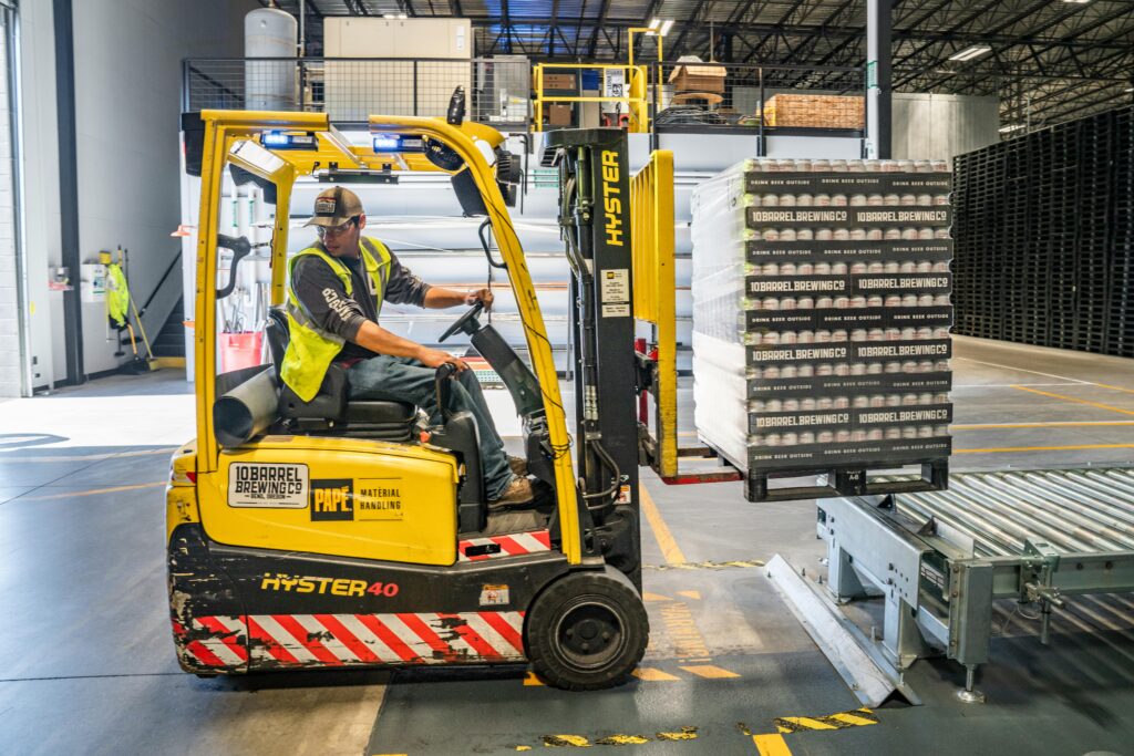 pexels-photo-1267338-1267338-1 A warehouse worker maneuvers a forklift to transport crates for brewing company storage.